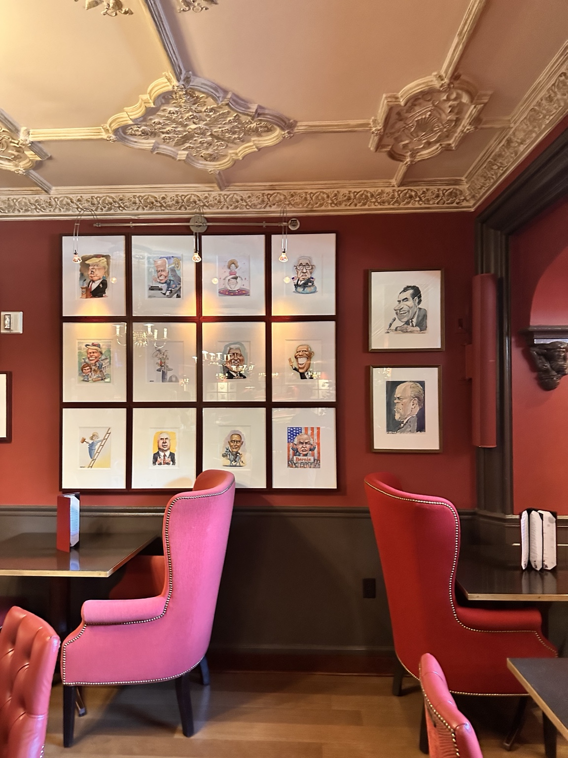 A dining room with pink chairs and framed portraits